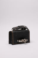 Clutch MCQUEEN in denim con dettagli decorativi a teschio e chiusura iconica.