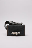 Clutch MCQUEEN in denim con dettagli decorativi a teschio e chiusura iconica.
