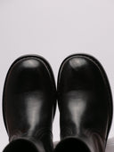 Stivaletti RAF SIMONS in pelle lucida nera, visione da diverse angolazioni mostrando graffi e dettagli strutturali.